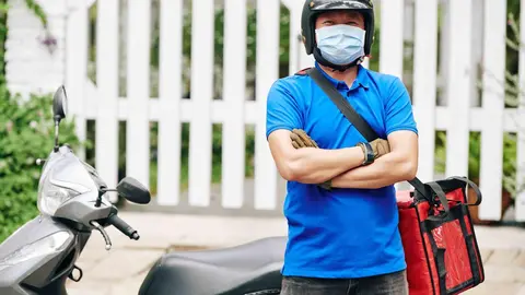 Portrait of happy confident delivery man standing at scooter with big cooler bag full of products
